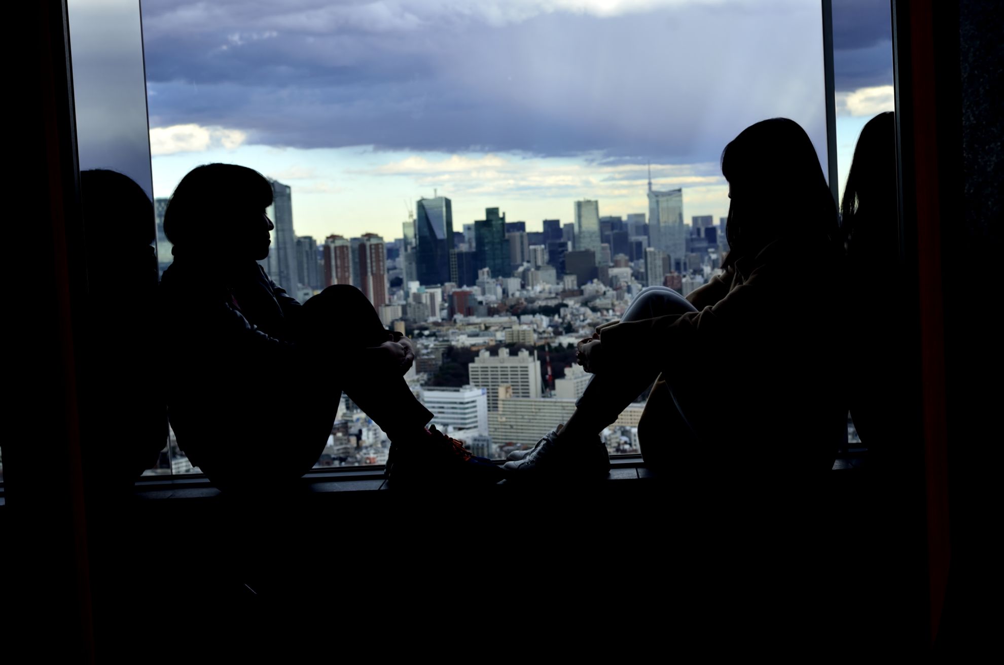 高層階の窓辺で向き合う二人のシルエットと都市の風景