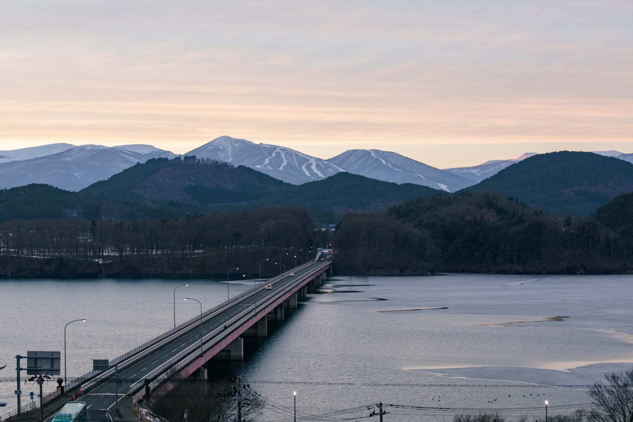 夕暮れの湖を渡る長い橋と山並み