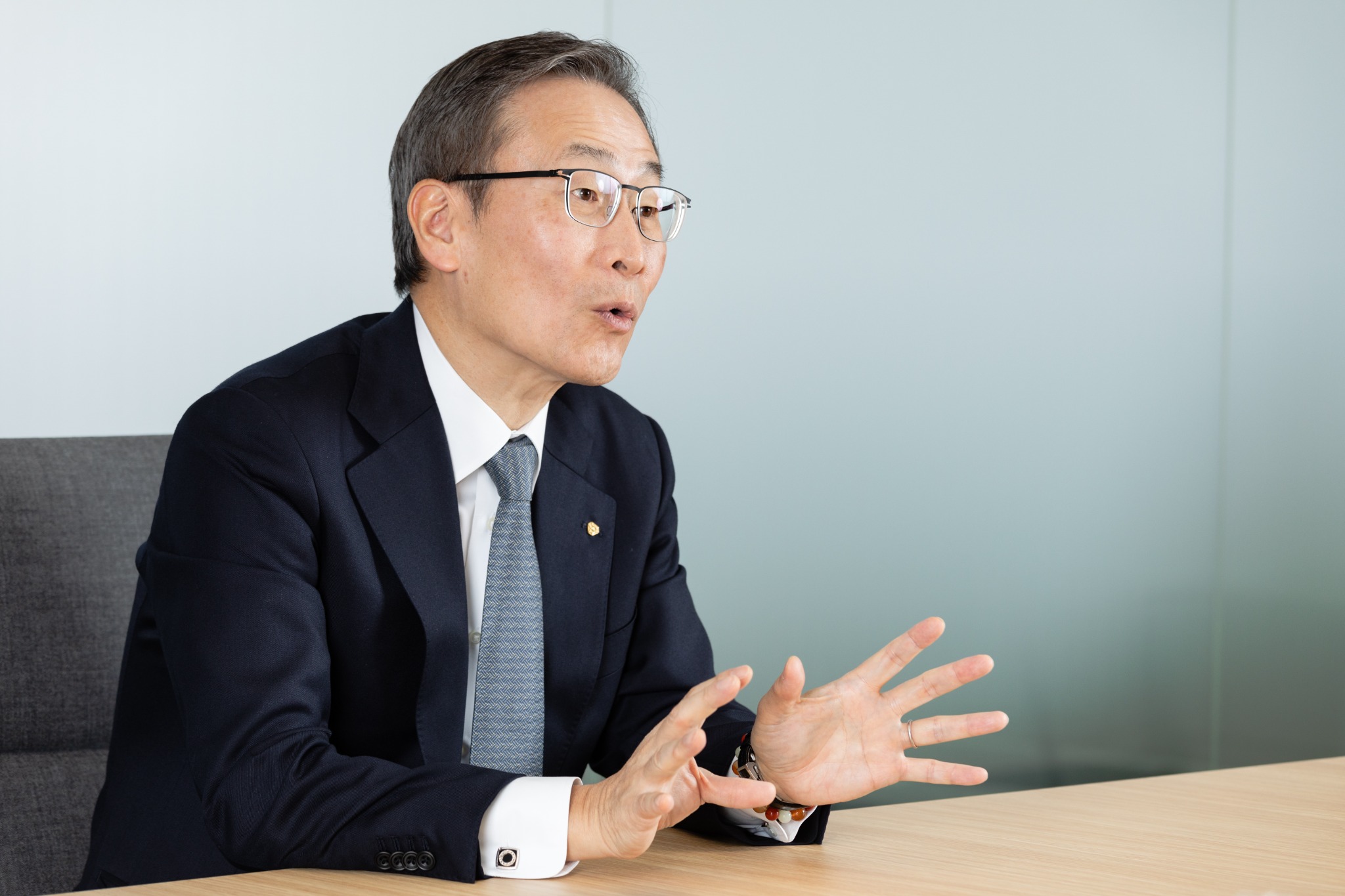 淡いブルーの背景で身振りを交えて語る企業経営者