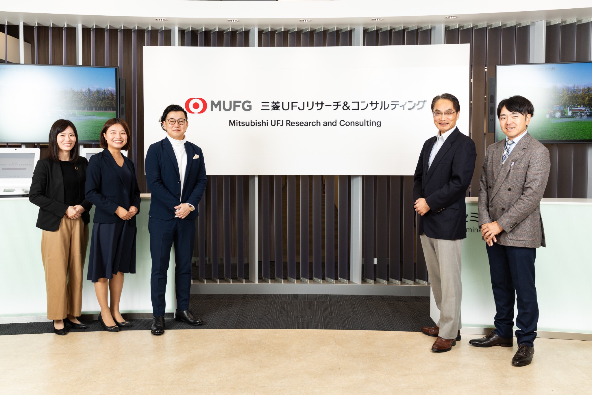企業ロゴの前に並ぶ取材参加者の集合写真