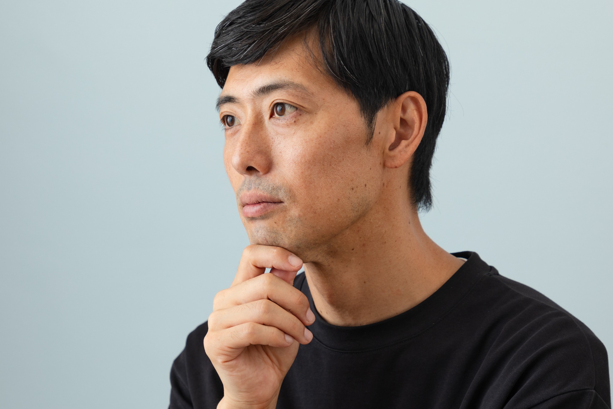 淡いブルーの背景で思案する人物の横顔
